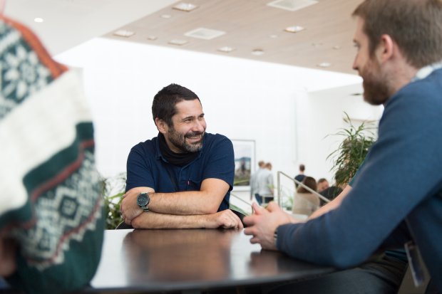 Smiling man sitting by a table while talking to colleagues