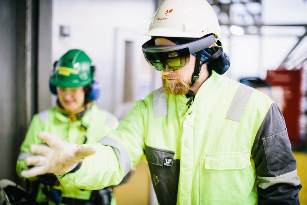 Photo of a man wearing protective gear and Microsoft Hololens glasses while making hand gestures in the air on an offshore oil rig