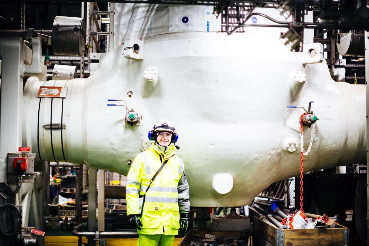 Photo of a person in protective gear standing in front of a massive valve