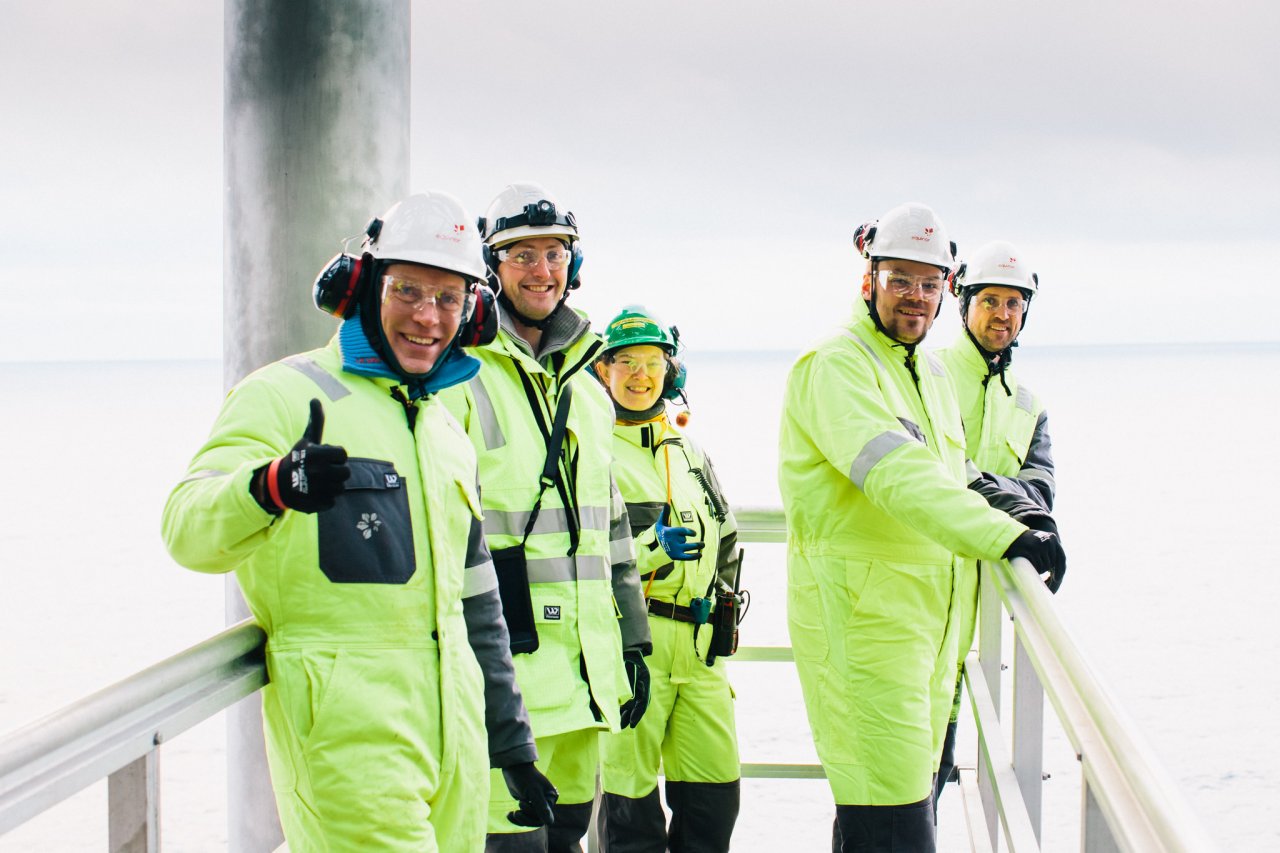 Photo of a group of smiling people standing on a ledge on an offshore oil rig, while wearing protective gear