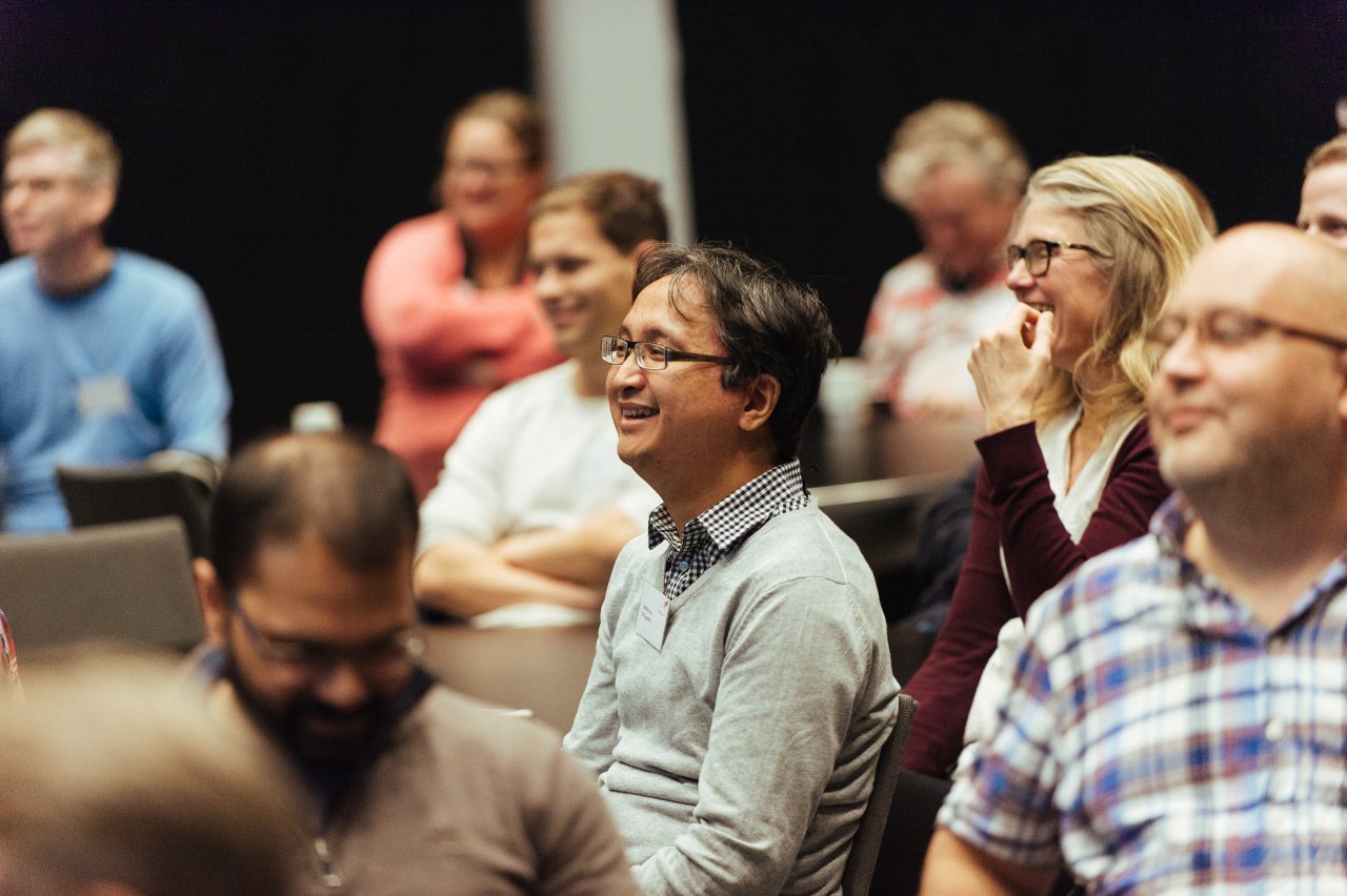 Photo of a smiling man sitting in a crowd of people during a conference