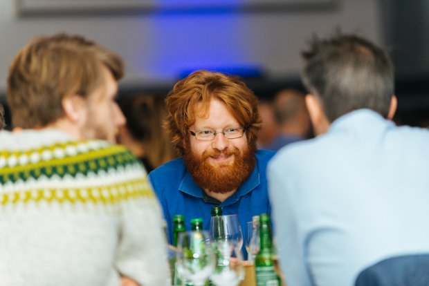Man smiling during a dinner conversation with colleagues at Equinor's own software developer conference, EDC