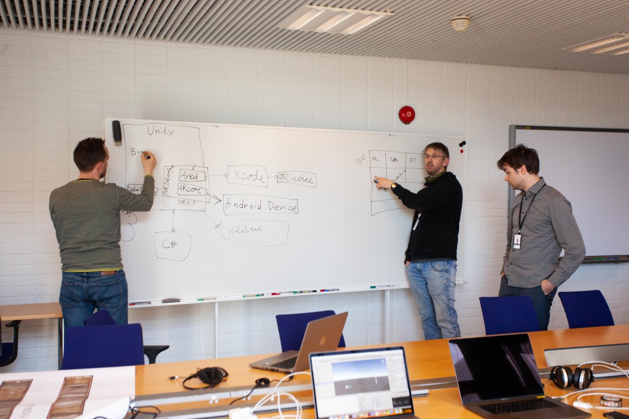 Three men writing something on a white board