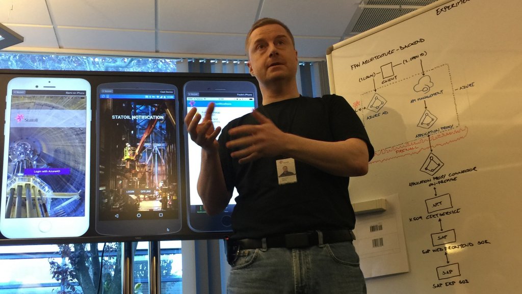 A man standing in front of a large screen and whiteboard while giving a presentation