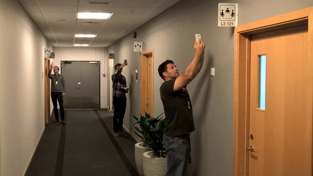 Three people taking photos of something on the wall in a hallway