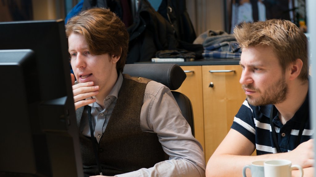 Two men sitting by a desk and working on something on a computer